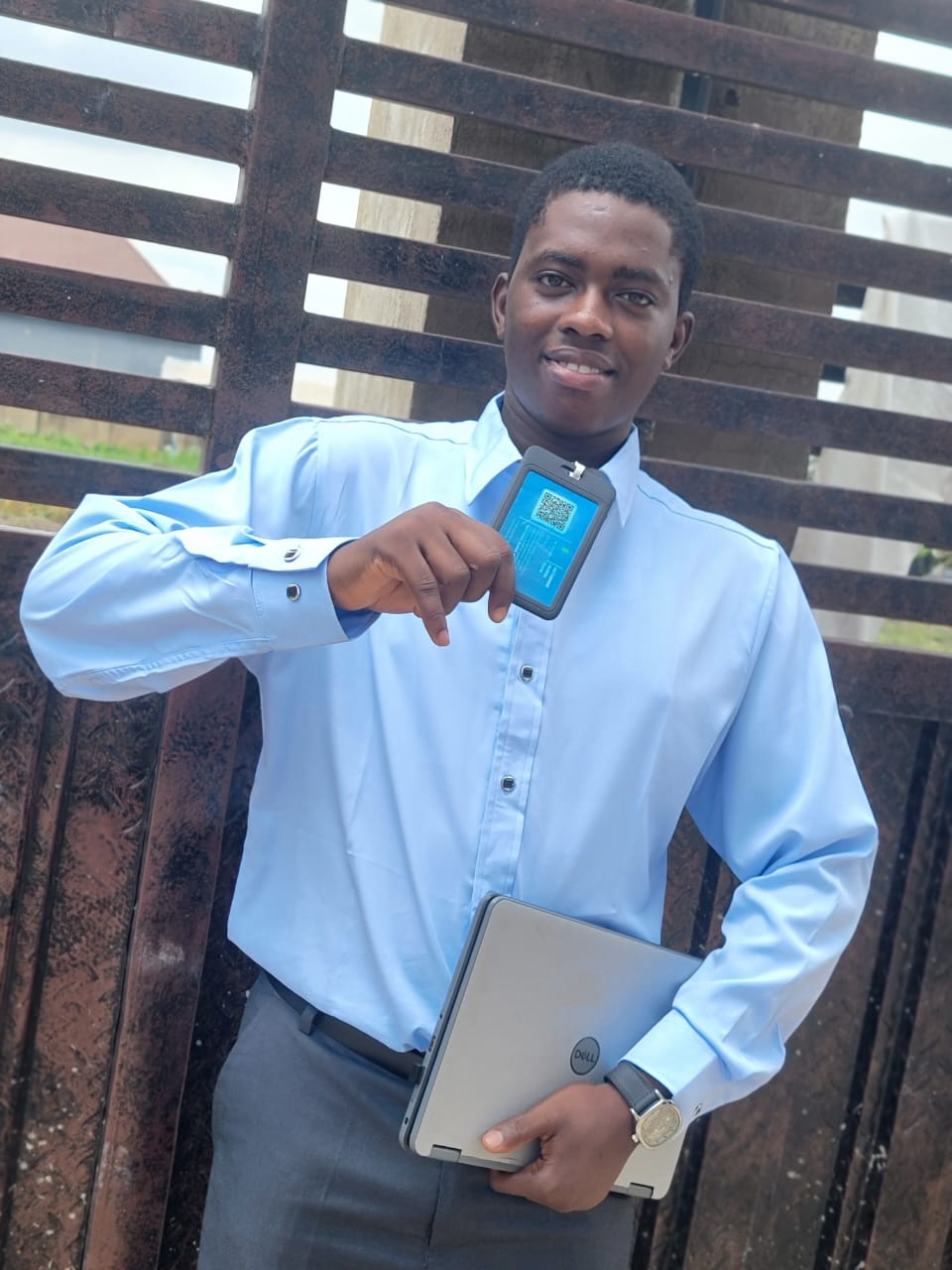 Fawaz Olayinka in a light blue shirt holding a laptop and his ID card